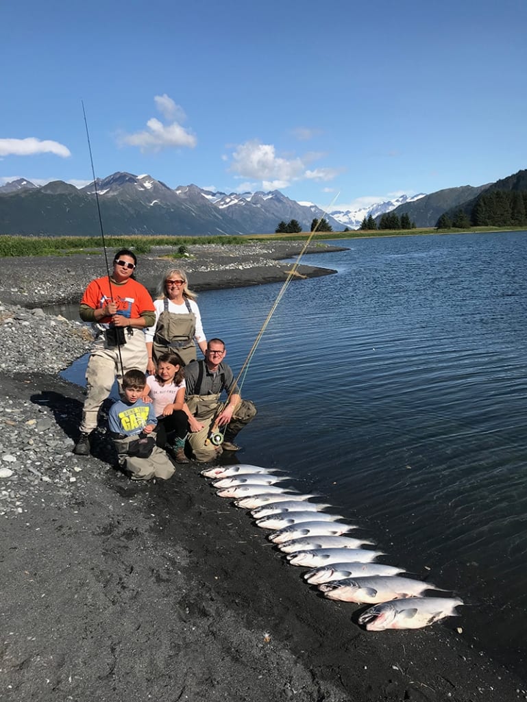 An Alaska fishing vacation is fun for the whole family and kids of all ages. Family displaying their catch waterside