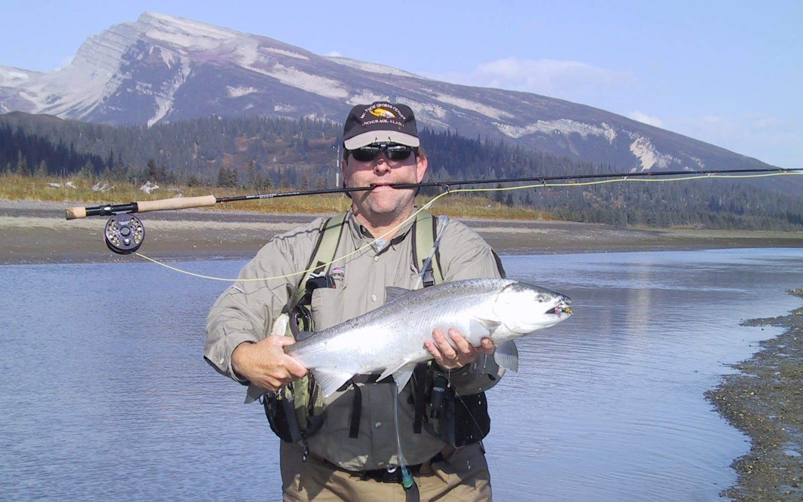 A man holds up a large salmon caught on a fly rod.