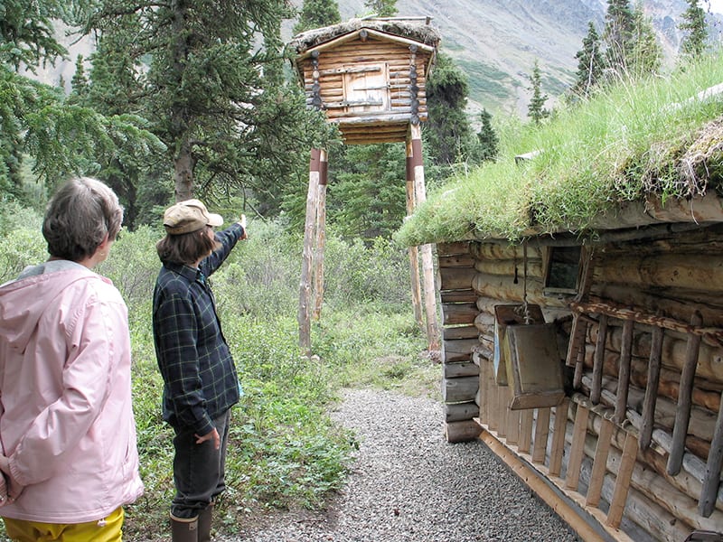 Visitors examine a cabin on a raised structure next to Dick Pronneke's main cabin.