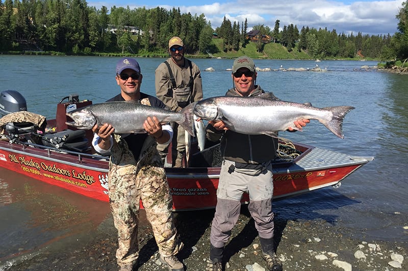 two men holding up king salmon in front of a boat