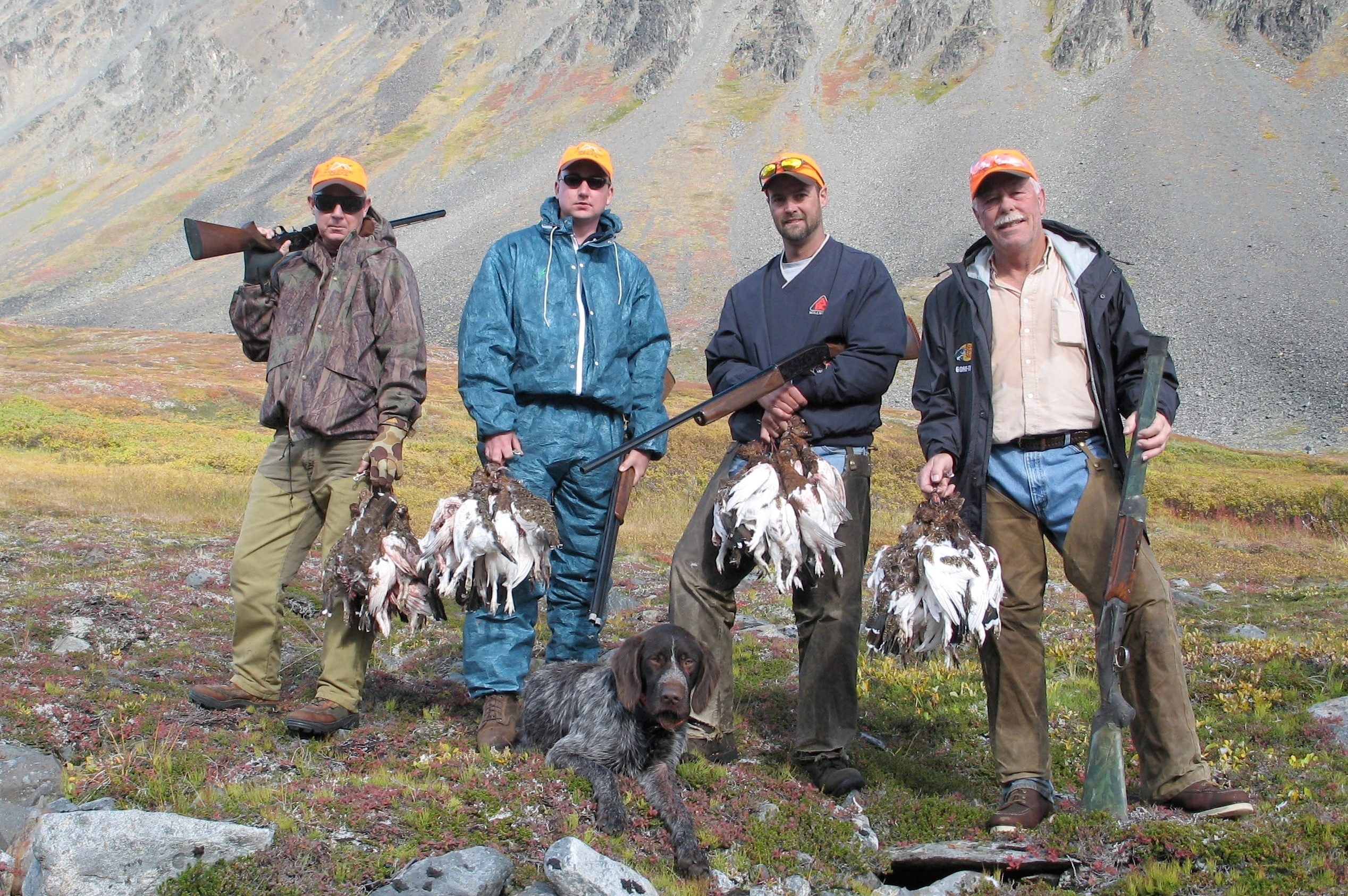 Four hunters and a dog post with their birds in front of a mountain peak.