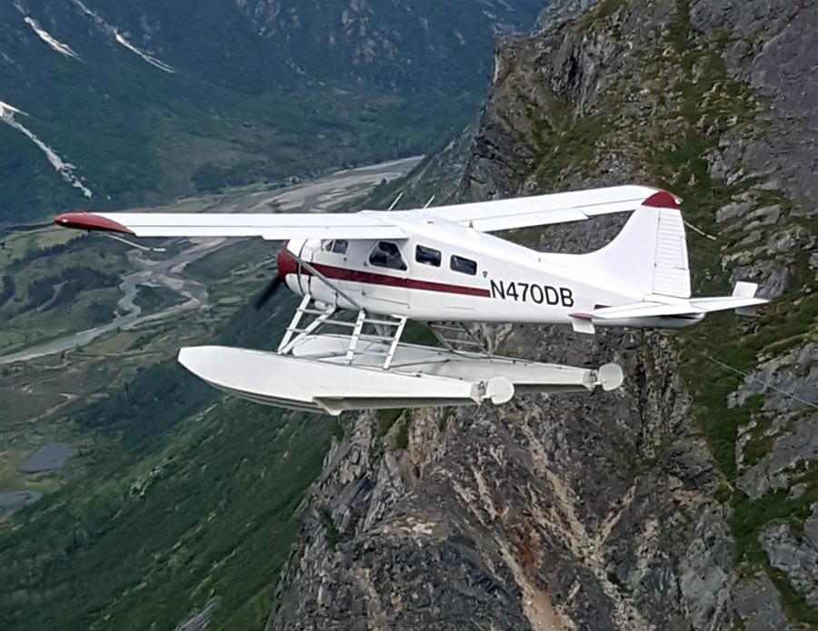 A float plane carves through the sky between mountain peaks.