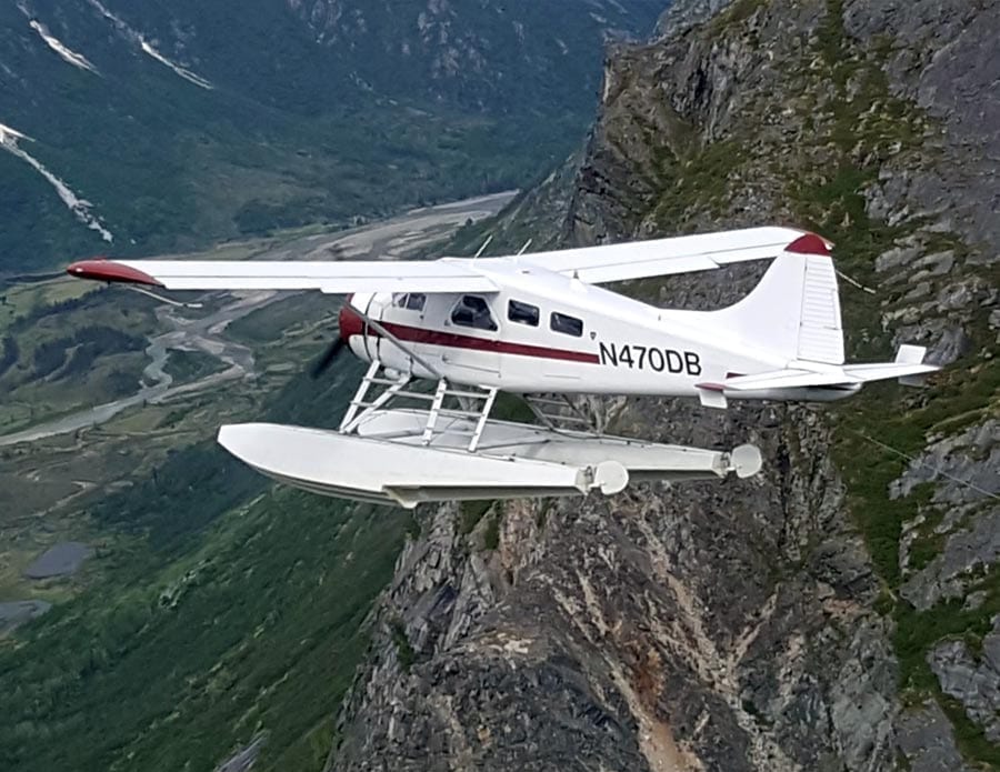 Enjoy stunning views from the window of our floatplane, then enjoy fishing unspoiled rivers and lakes. A float plane carves through the sky between mountain peaks.