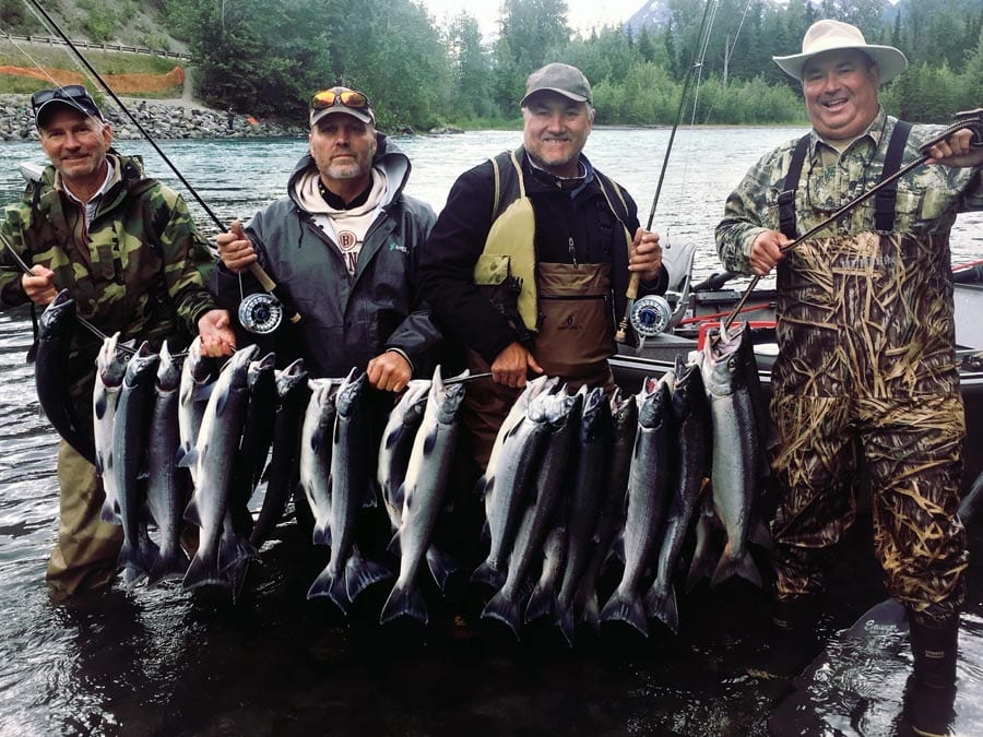 Four anglers hold many salmon on a stringer.