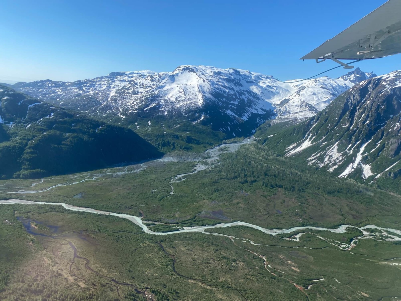 Beautiful scene of a river cutting through green land at the base of snowy mountains.