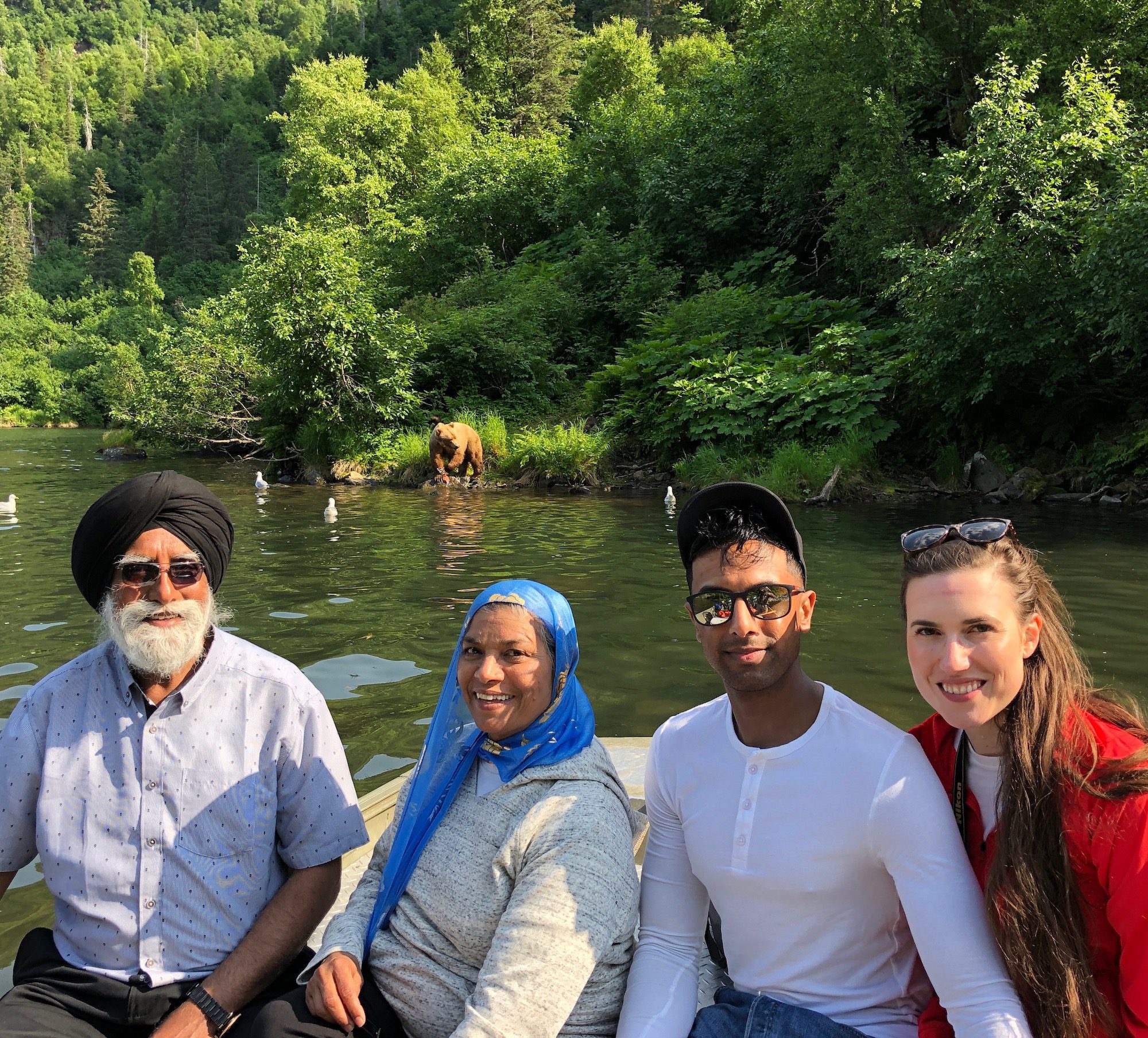 A group of people pose for a picture on a boat in front of a photobombing brown bear.