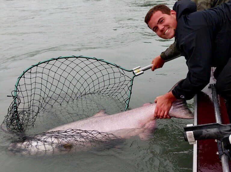 single-angler-posing-caught-net-king-salmon-fish-boat-2022-3-17 Angler lifting up his king salmon catch in a fishing net.