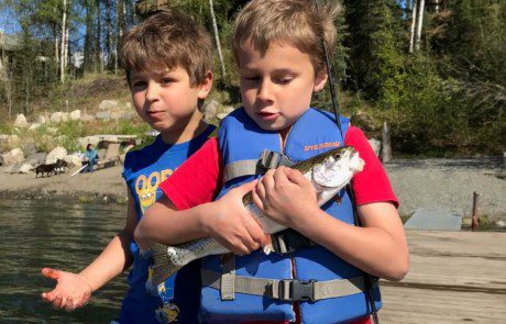 group-angler-child-posing-rainbow-trout-fish-bank-2022-3-17 Two children on a dock, one holding close the rainbow trout he caught.
