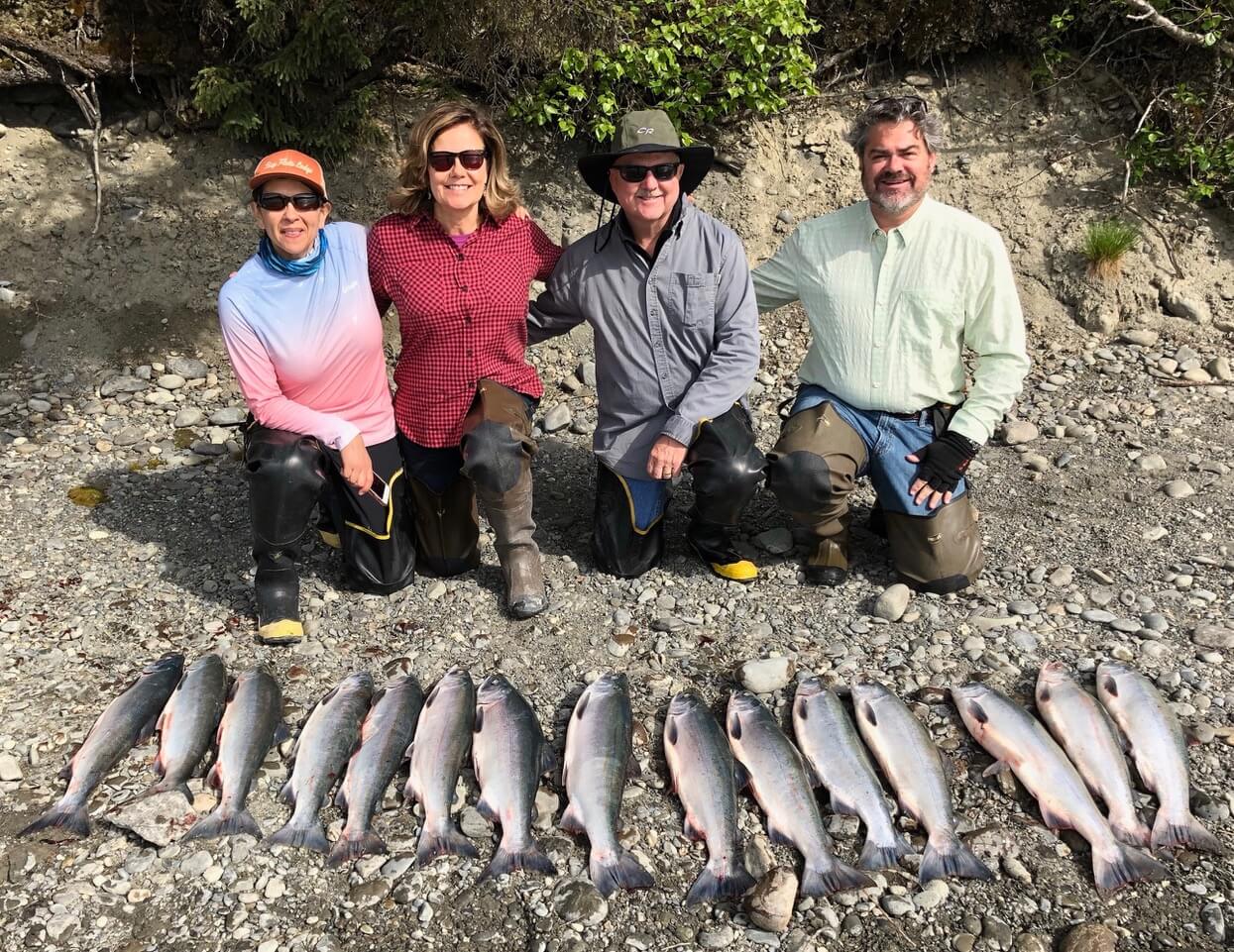 Four anglers posing on the shore in front of a line of caught king salmon.