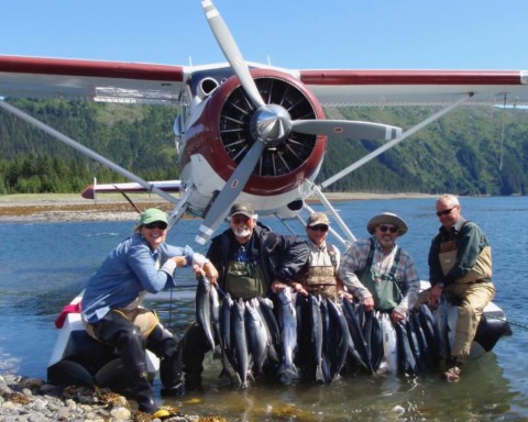 A group of anglers displaying their catch of silver salmon in front of the plane.