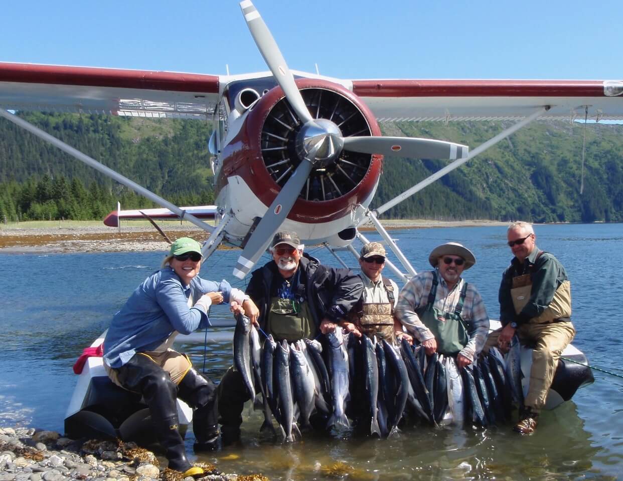 A group of anglers displaying their catch of silver salmon in front of the plane.