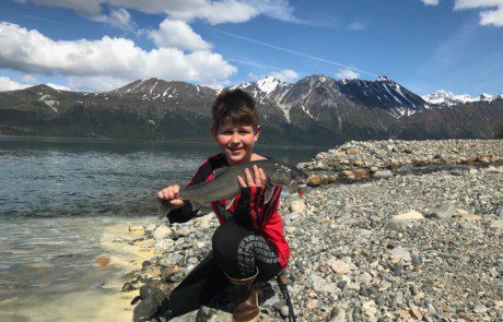 single-angler-child-posing-lake-trout-fish-bank-2022-3-17 A child at the edge of a river displaying the lake trout he caught.