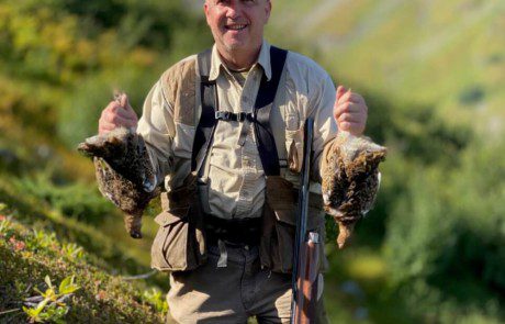 single-hunter-posing-ptarmigan-bird-2022-5-13 A hunter happily displaying a couple of ptarmigan grouse on a hillside.