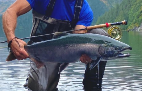 single-angler-posing-silver-salmon-fish-2022-5-13 An angler standing in the river against a lovely mountain backdrop holding the silver salmon he caught.